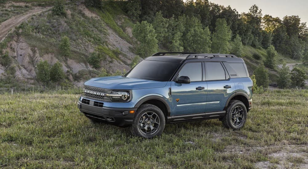 A blue 2021 Ford Bronco Sport is parked in front of a tree-covered hill.