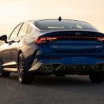 A blue 2021 Kia K5 is shown from the rear during a yellow sunset.