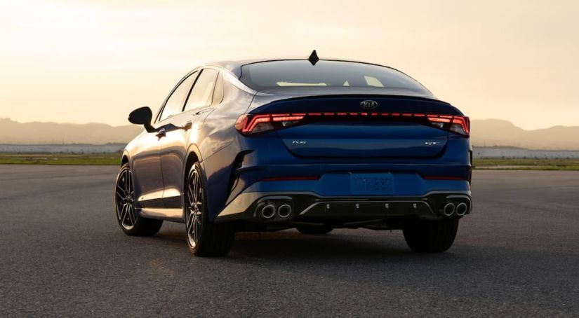 A blue 2021 Kia K5 is shown from the rear during a yellow sunset.