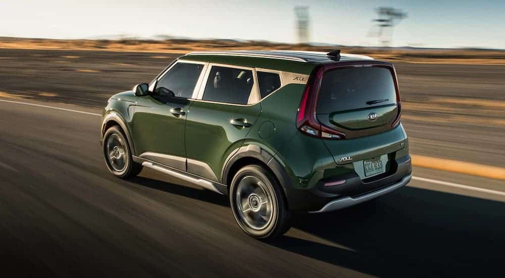 A green 2021 Kia Soul is driving away on a desert road.
