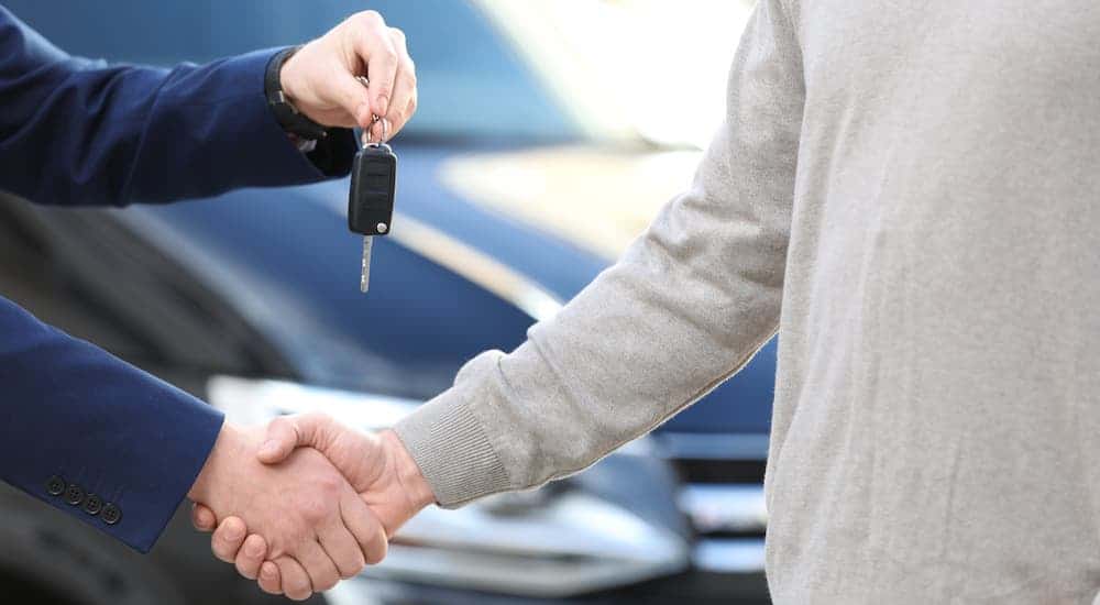 Two hands are shaking and handing over car keys in front of a black car,