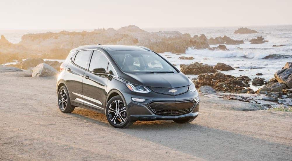 A gray 2020 Chevy Bolt EV is parked on a beach at sunset.