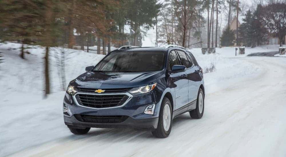 A dark blue 2020 Chevy Equinox from a local Chevy dealer is driving on a snow-covered road.
