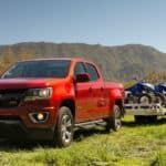 A red 2020 Chevy Colorado is parked in a field with a trailer and several four wheelers.