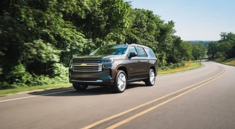A brown 2021 Chevy Tahoe, soon to be hitting a GM Dealer near you, is driving on a tree-lined highway.