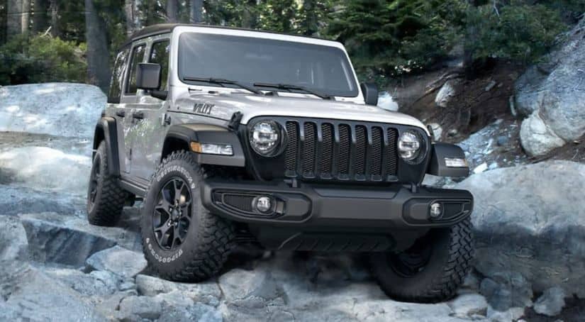A silver 2020 Jeep Wrangler Unlimited Willys edition is off-roading on rocks after leaving a Jeep dealer near me.