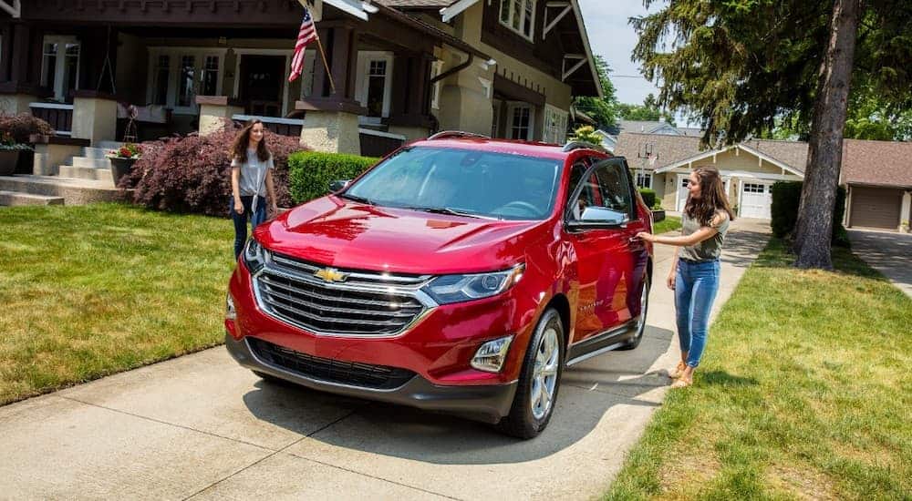 Two girls are walking up to a red 2018 Chevy Equinox in the driveway of a brown house.