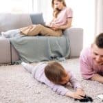 Two boys are playing with toy cars in front of woman who is shopping on a laptop at an online car dealership.