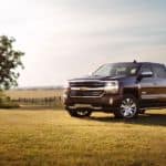 A crowd favorite at used car dealerships, a black 2017 Chevy Silverado 1500 High Country, is shown parked next to a tree in a field.