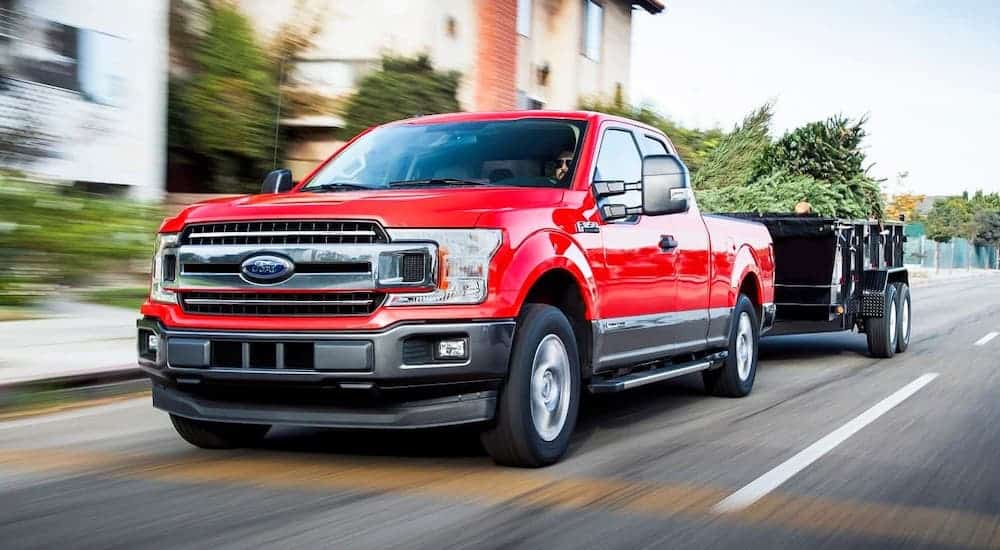 A red 2017 Ford F-150 is towing a trailer on a suburban road.