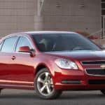A red 2010 Chevy Malibu is parked in front of a modern building.