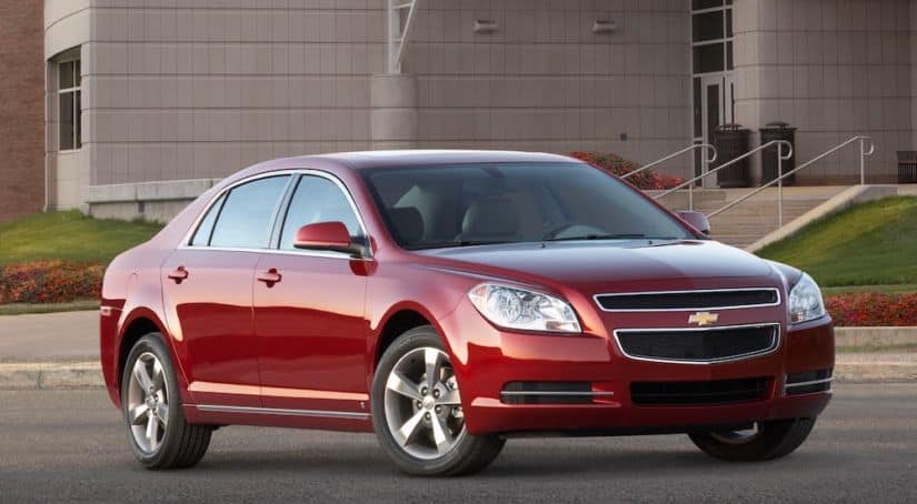 A red 2010 Chevy Malibu is parked in front of a modern building.