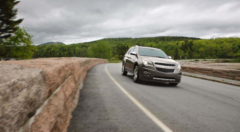 A popular used car for sale, a gray 2014 Chevy Equinox, is driving on an empty highway.