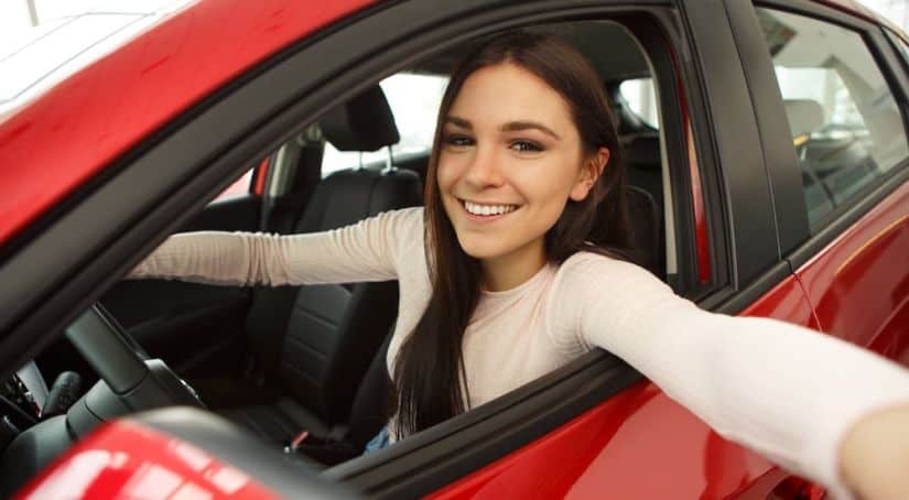 A young woman is reaching out of the driver's seat in a red car.