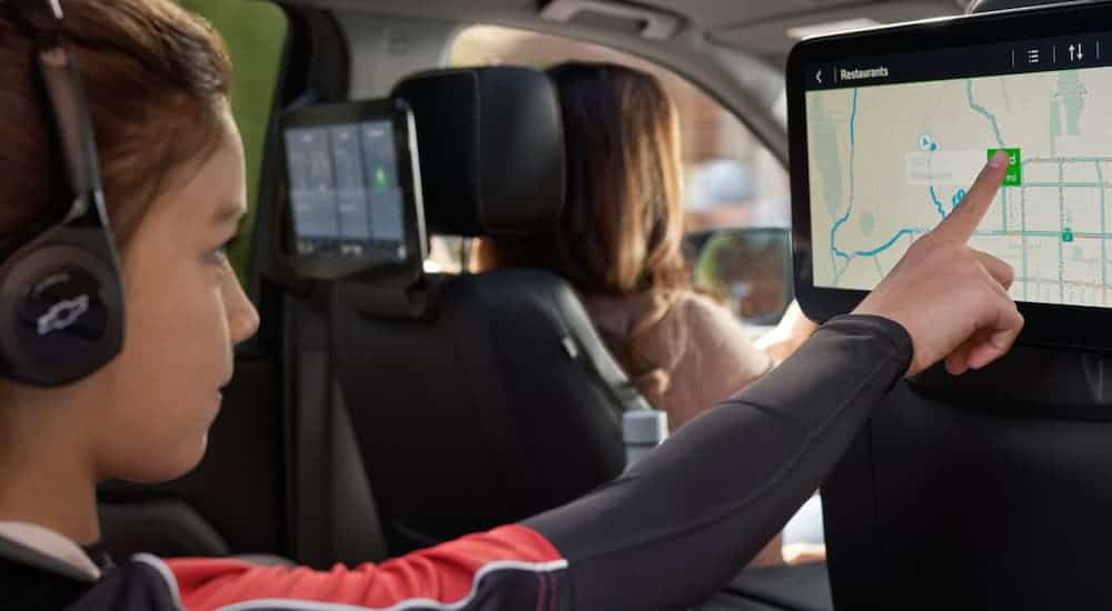 The rear media system of a 2021 Chevy Suburban is shown with a girl looking up directions to a pizza place, after leaving a Chevy dealership near you.
