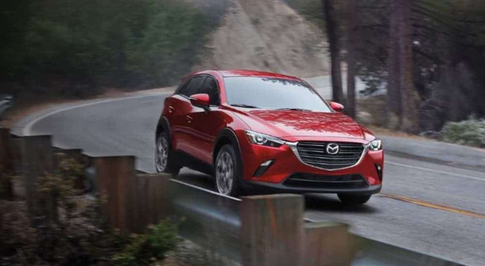 A red 2020 Mazda CX-3 is driving around a corner on a rural road.