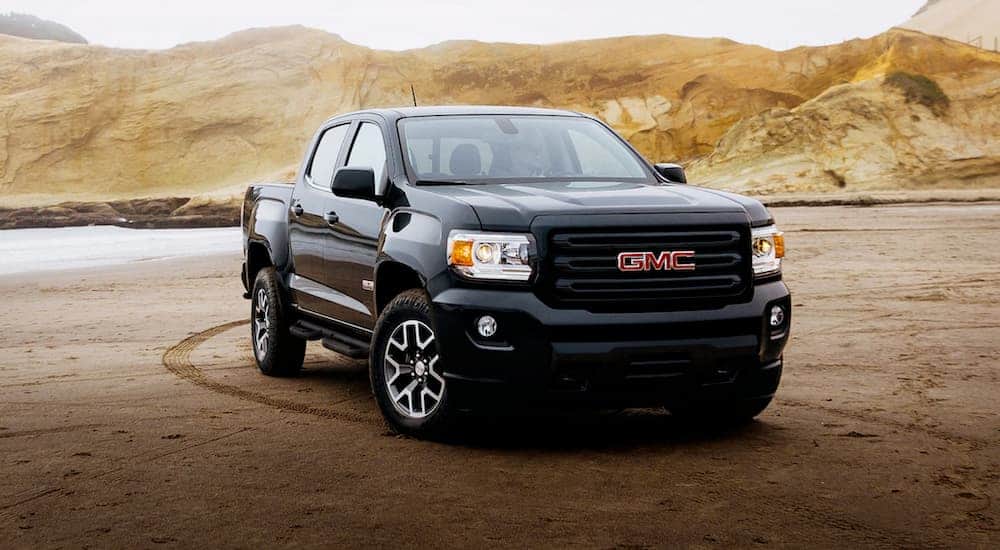 A black 2020 GMC Canyon is parked in the sand at a beach.