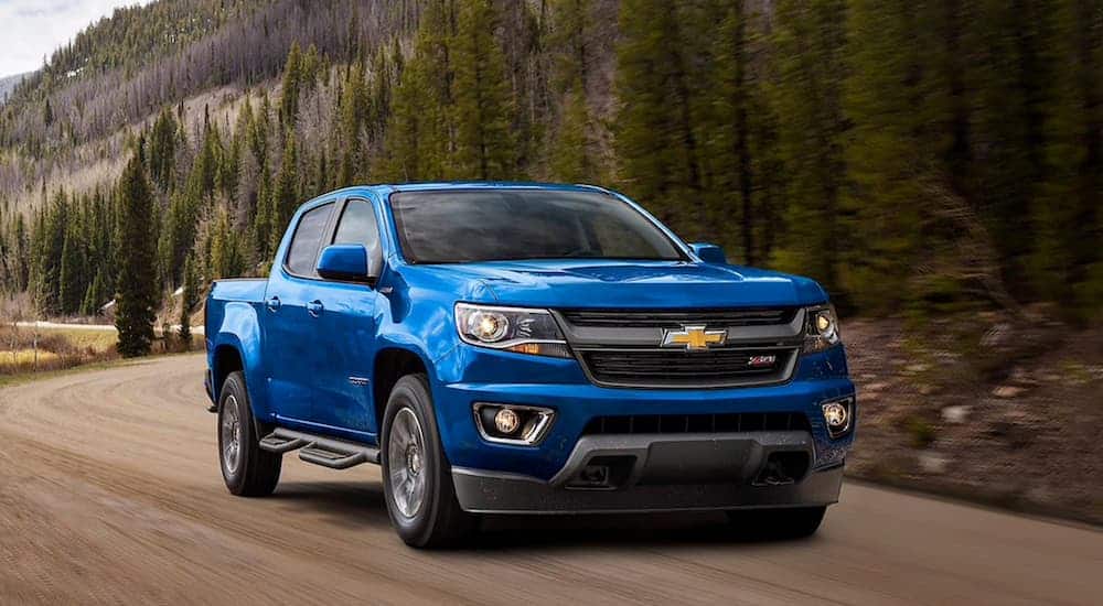 A blue 2020 Chevy Colorado is driving on a dirt road past pine trees.