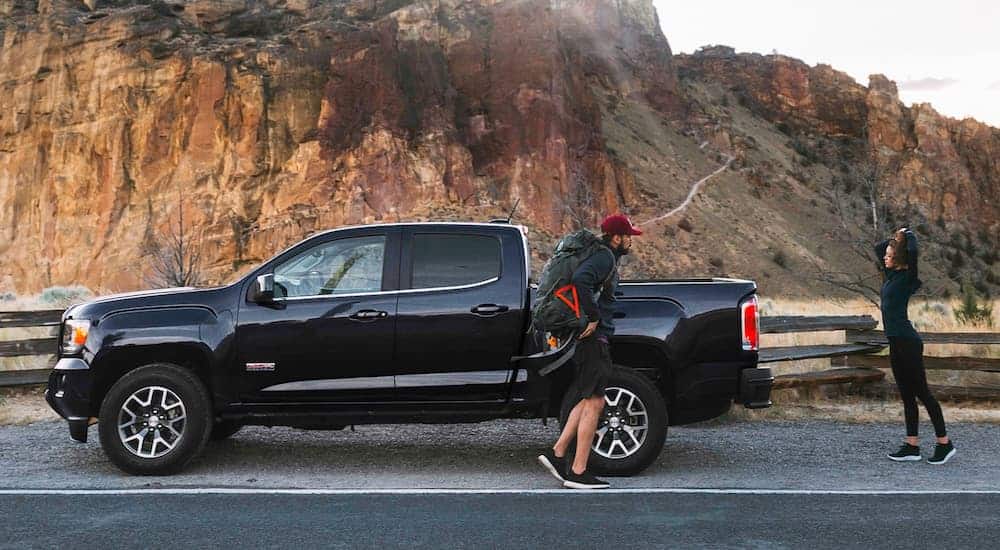 A couople is walking away from a black 2020 GMC Canyon to hike desert mountains.