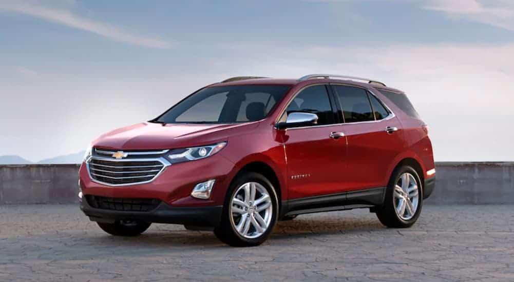 A red 2020 Chevy Equinox is parked in front of a low stone wall and blue sky.