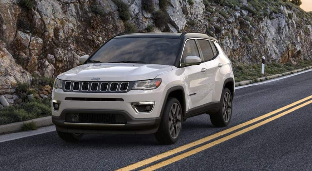 A white 2020 Jeep Compass is driving past rock face.