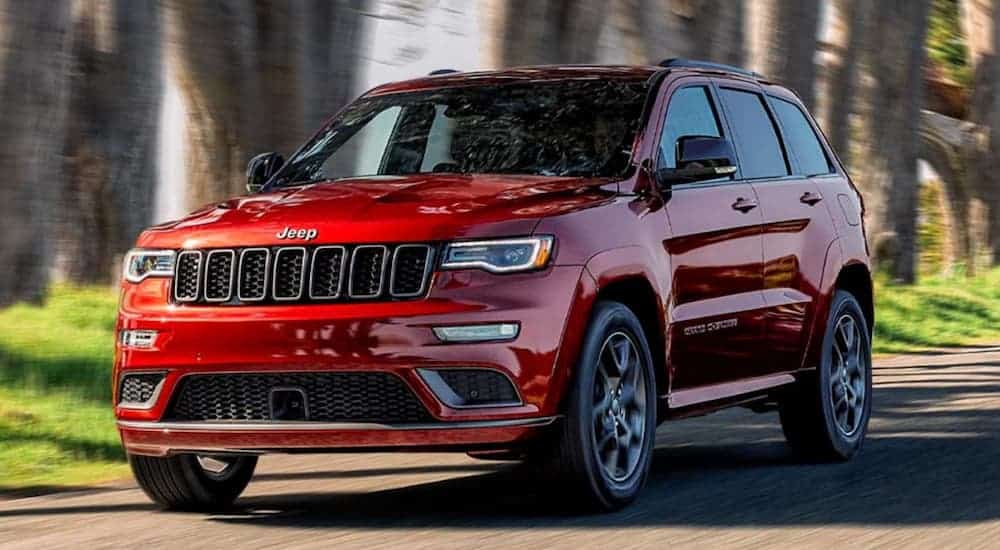 A red 2020 Jeep Grand Cherokee is driving on a tree-lined street.