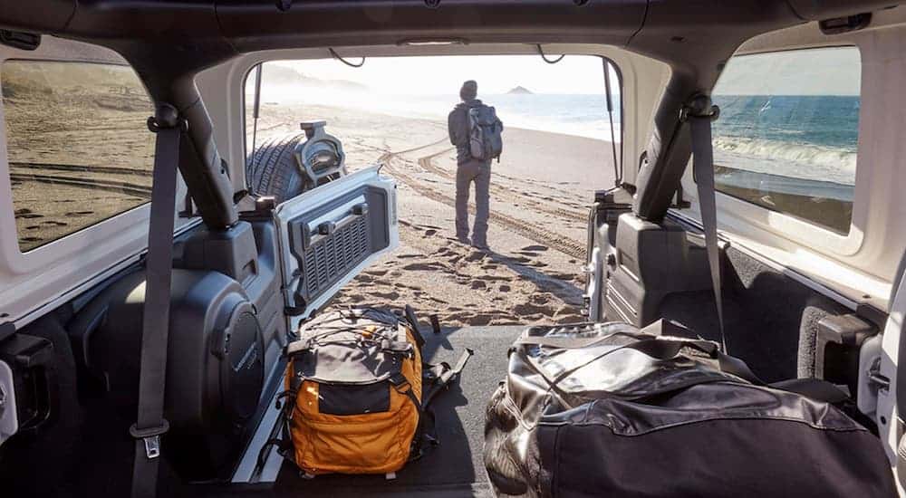 Gear and bags are in the cargo area of a 2020 Jeep Wrangler with a view looking out to a man on the beach.