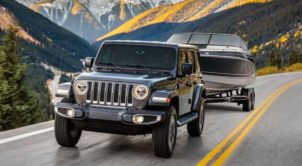 A grey 2020 Jeep Wrangler Unlimited is towing a boat on a mountain road.