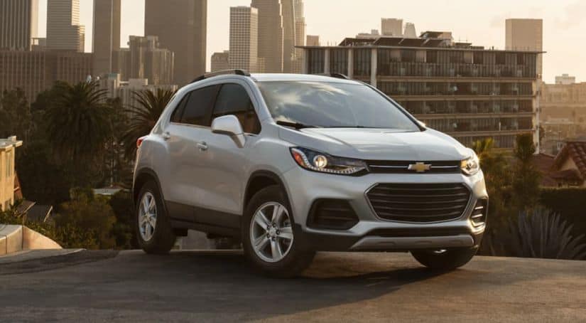 A white 2021 Chevrolet Trax is parked on a city street in front of a city skyline at sunrise.