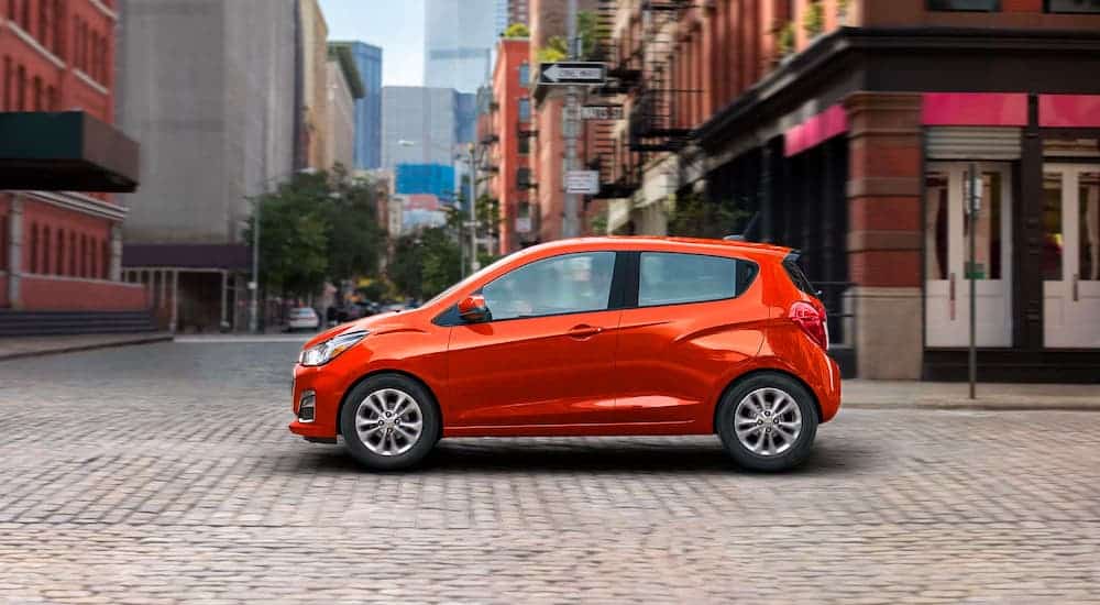 A red 2021 Chevy Spark is shown from the side driving on a cobble stone road.