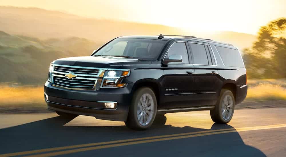 A black 2020 Chevy Suburban is driving past hills at sunset.