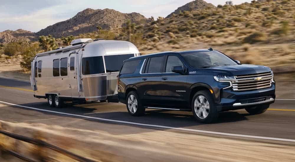 A blue 2021 Chevy Suburban is towing an Airstream past hills.