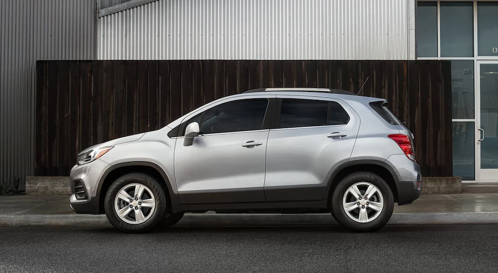 A sliver 2021 Chevy Trax is shown from the side in front of a black and silver building.