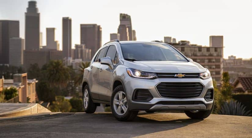 A silver 2021 Chevy Trax is parked in front of a city skyline.
