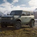 A green 2021 Ford Bronco (4dr) is parked on grass in front of distant mountains.