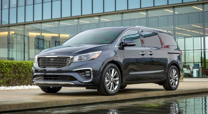 A blue 2021 Kia Sedona is parked in front of a modern building near water.