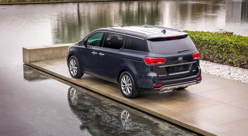 A blue 2021 Kia Sedona is parked on a concrete jetty surrounded by water.