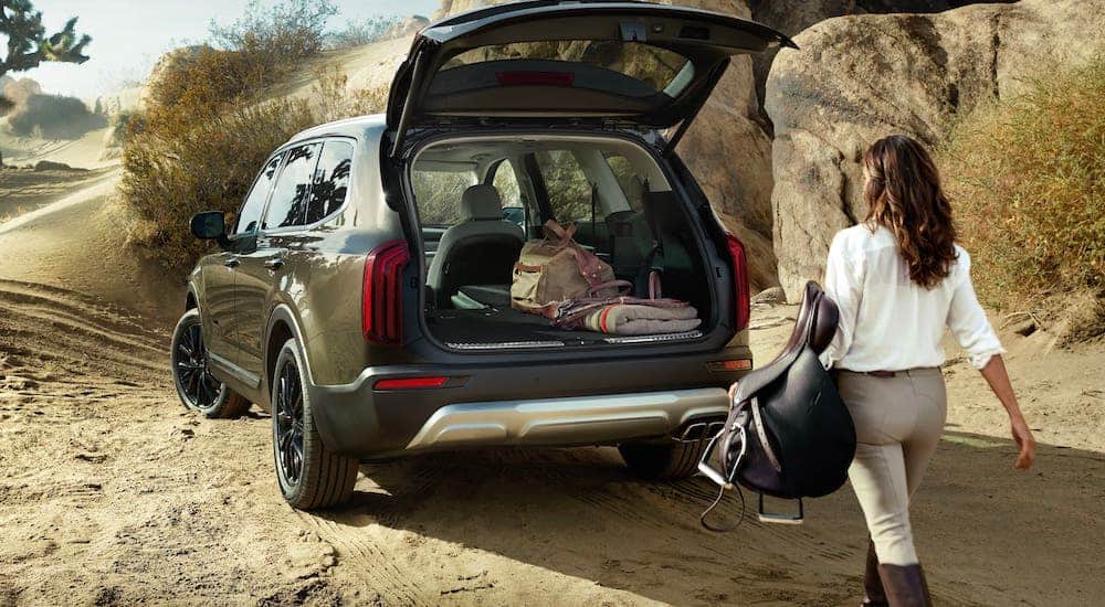 A woman is loading equestrian gear into the back of a green 2021 Kia Telluride.