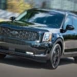 A black 2021 Kia Telluride is driving on a street.