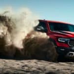 A red 2021 Ram 1500 TRX is shown angled right while off roading in the desert kicking up sand.