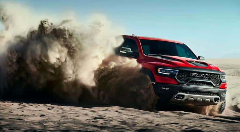 A red 2021 Ram 1500 TRX is shown angled right while off roading in the desert kicking up sand.