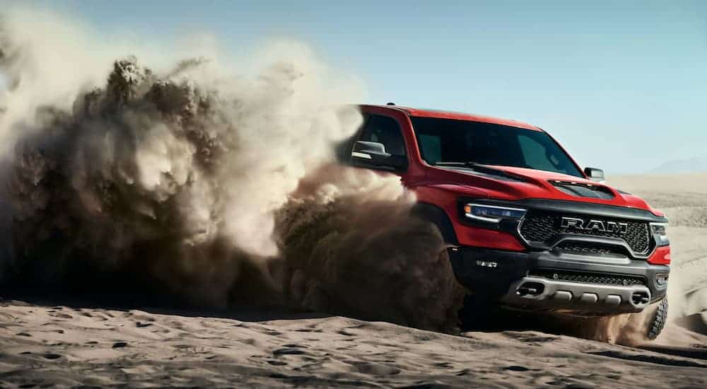 A red 2021 Ram 1500 TRX is kicking up sand while off-roading after winning the 2021 Ram TRX vs 2020 Ford Raptor comparison.