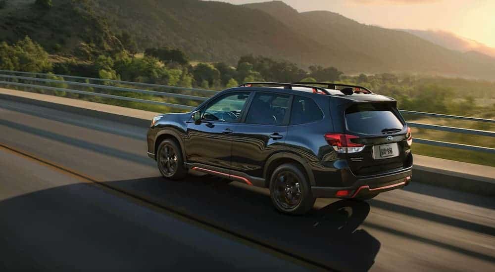 A black 2021 Subaru Forester is driving past mountains at sunset.