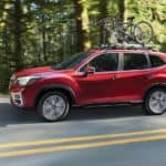 A red 2021 Subaru Forester is driving on a tree-lined road with bikes on the roof.