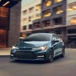A blue/gray 2021 Toyota Corolla is driving around a corner in a city.