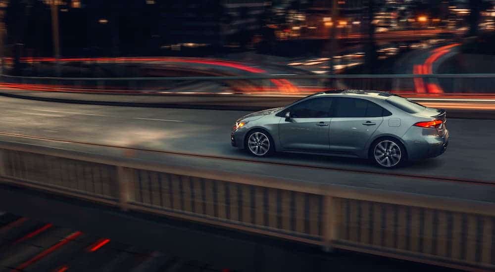 A gray 2021 Toyota Corolla is driving on a bridge at night.