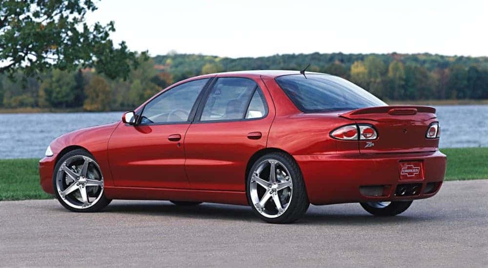 An older cheap car near you, a red 2005 Chevy Cavalier is parked in front of a river.