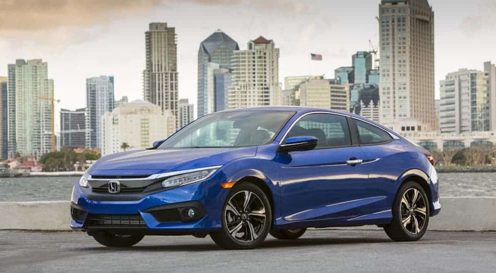 A blue 2018 Honda Civic is parked in front of a river and city.