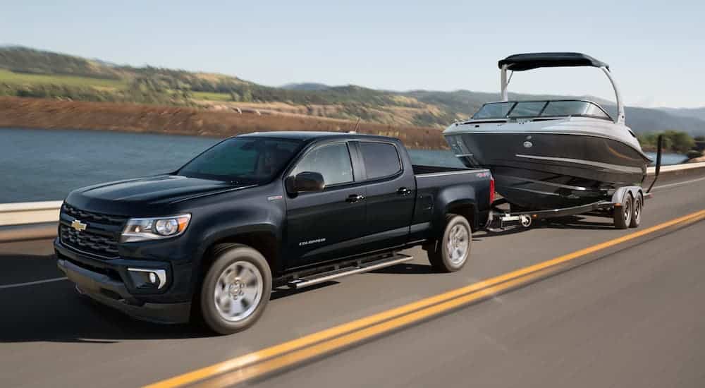 A black 2021 Chevy Colorado is towing a boat past a lake.
