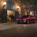 A red 2021 Chevy Malibu is parked in front of a tan brick building.